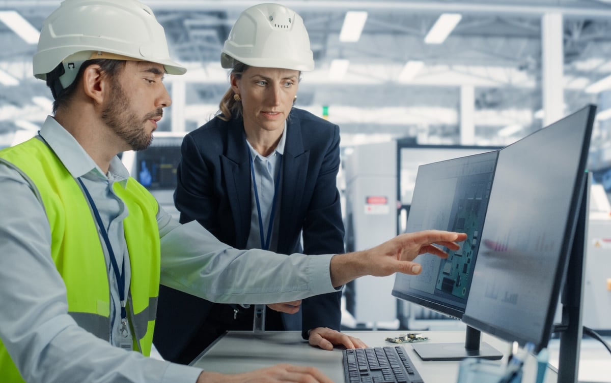 man-instruerar-kvinna-på dator-i-fabrik